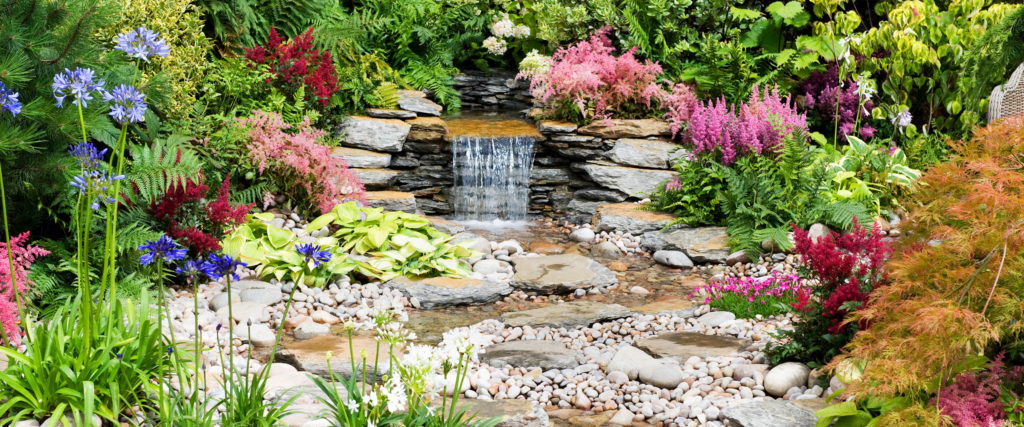 a backyard waterfall surrounded by flowering plants