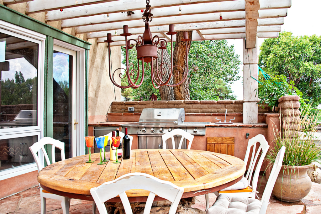 A patio off of the house with a build in exterior kitchen with counter top and gas grill with a dining table and chairs.