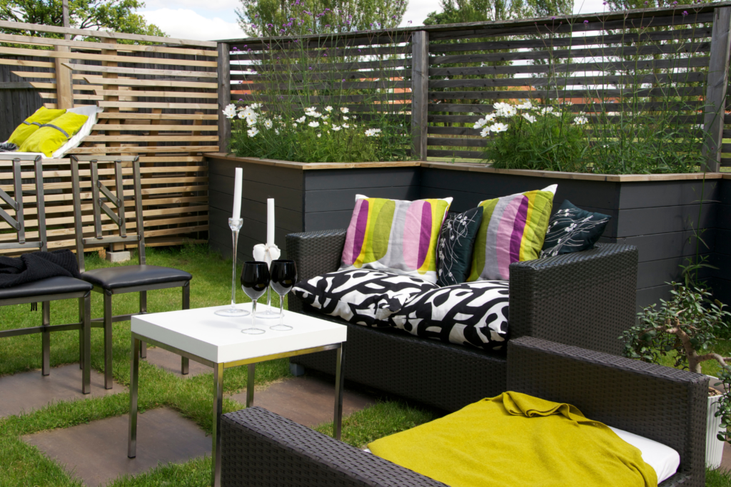 Patio furniture set with yellow pillows and surrounded by a privacy fence and small white table.