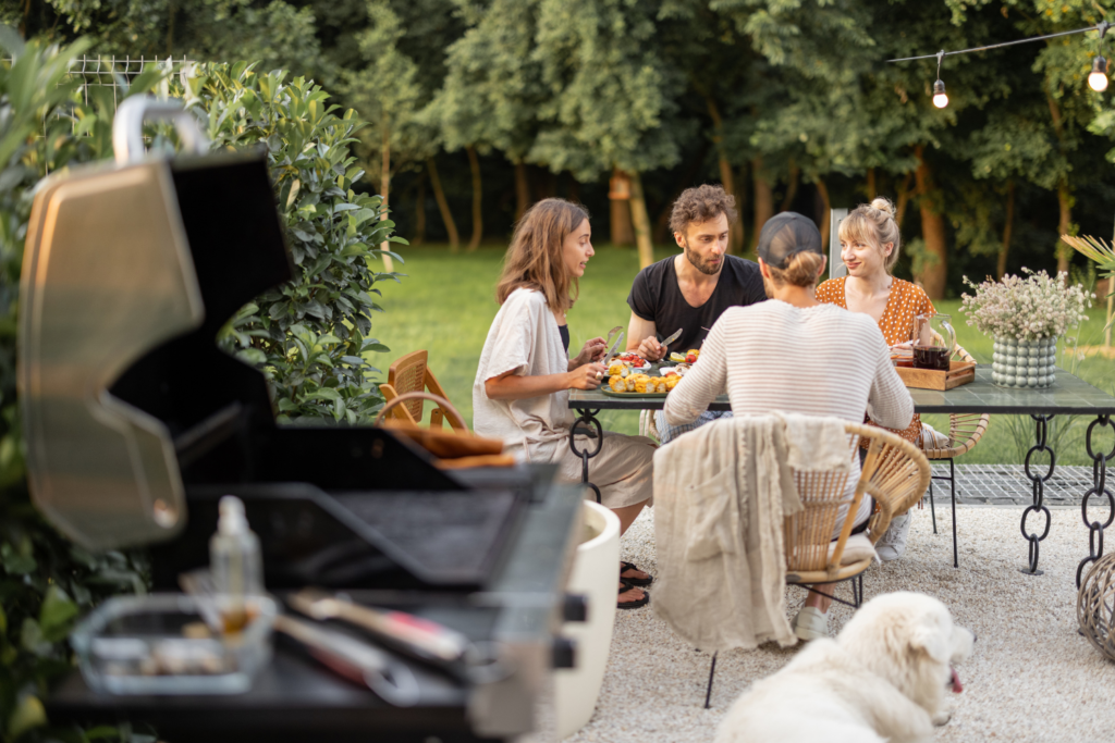 A family dining on their patio with a grill cooking meat