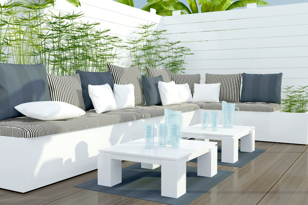 A white patio set in the L shape with blue striped cushion and blue and white pillows and a white coffee table in front and a white privacy fence behind the patio.