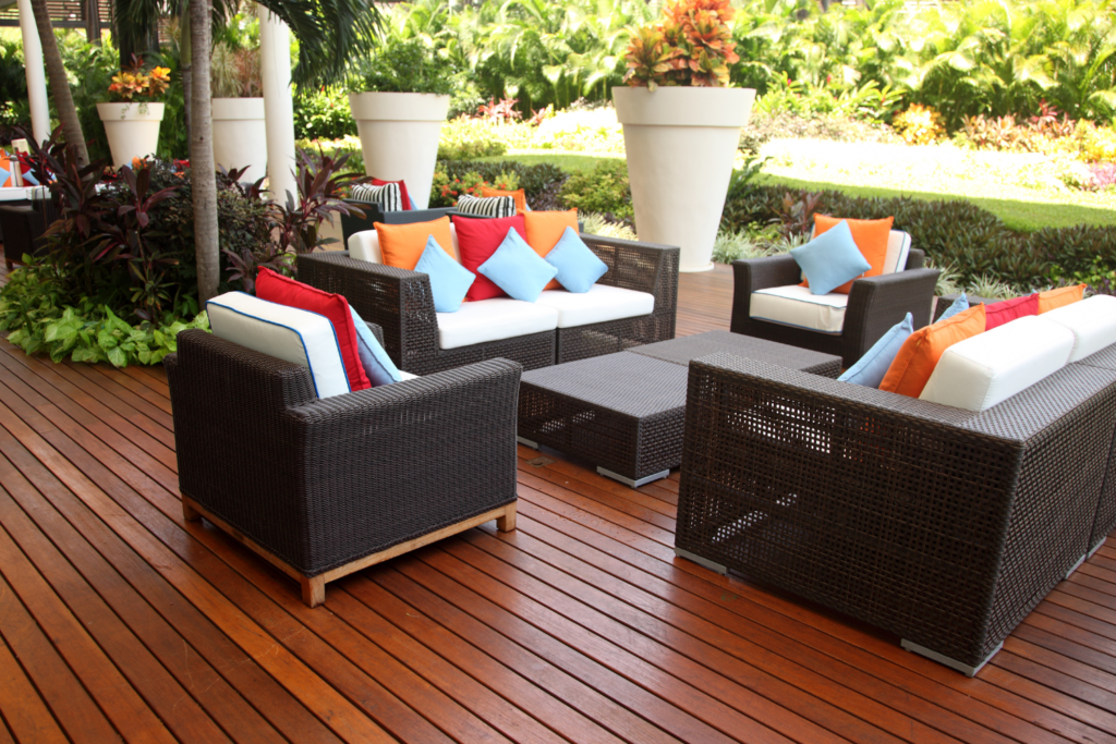 A wood deck patio with brown wicker furniture and white cushions and colorful pillows.