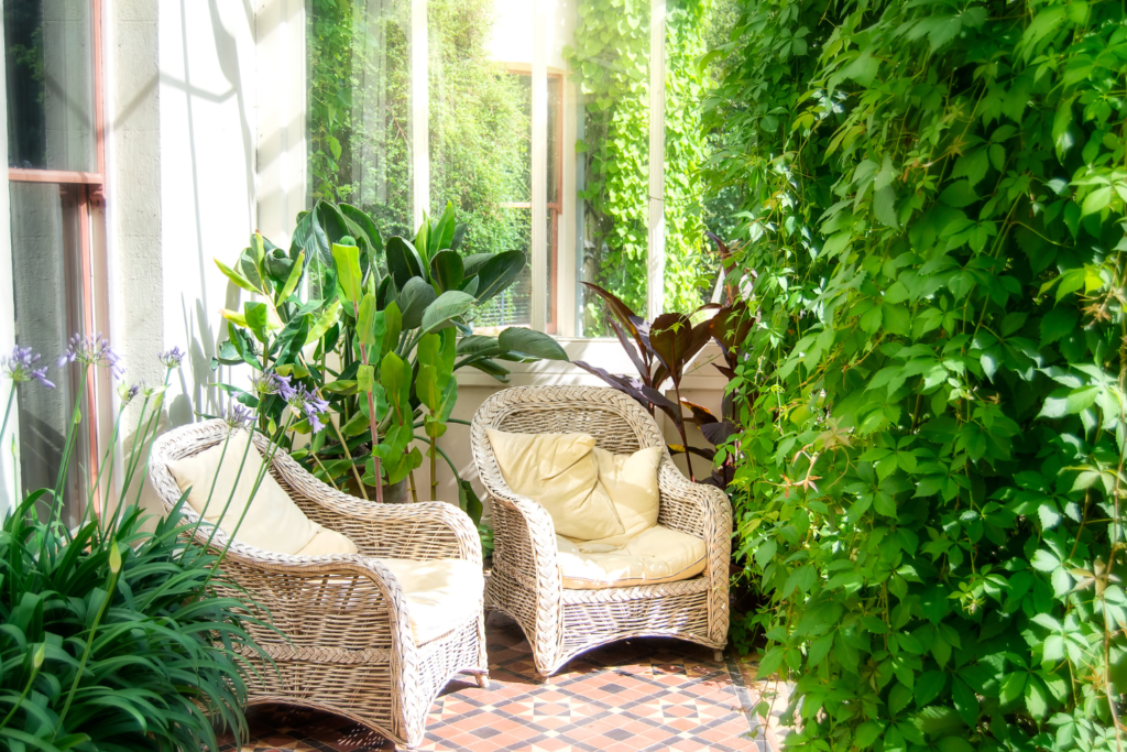 A private intimate patio design with white wicker furniture and green plants surrounding along with hanging ivy.