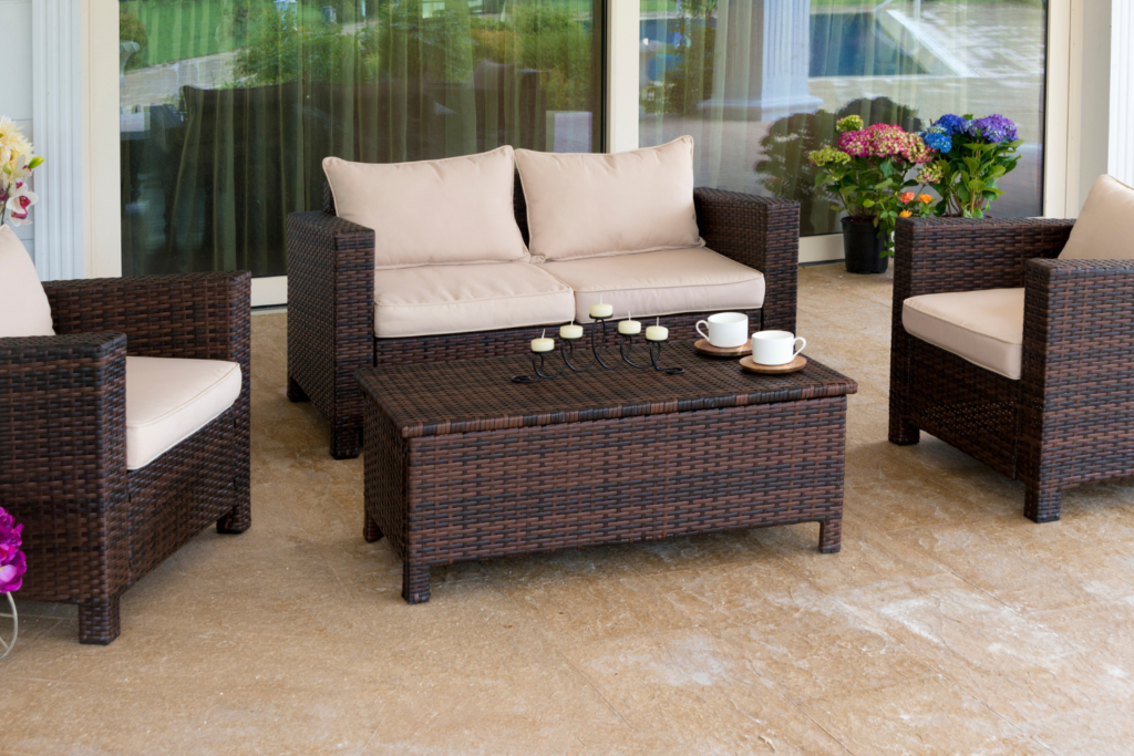 A patio off of sliding glass doors with brown wicker furniture and tan cushion pillows and a wicker table.