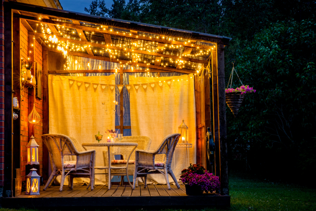 a porch on wood deck with patio table and chairs and string lighting hanging above