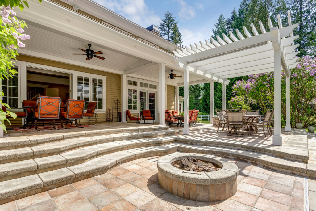 a white pergola on a tiled patio with rock and tile firepit.