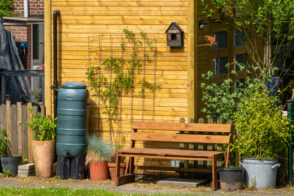 A wooden bench in front of a wood sided house with plants.