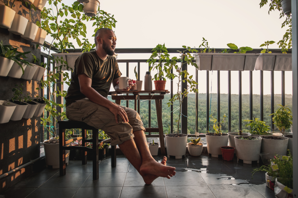 Man sitting on an apartment patio with vegetable plants and garden and flower garden