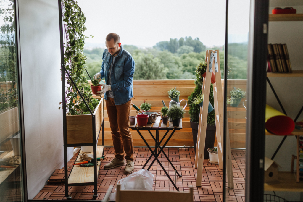 Man tending to a garden on a balcony patio with a folding table and vertical garden